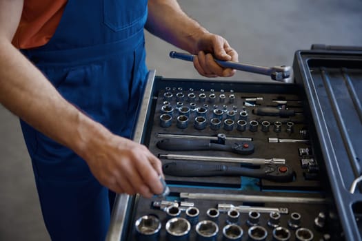 Closeup high angle view on tool box and male mechanic hands taking wrench for work cropped shot. Professional repairman service at auto garage