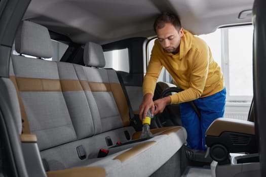Man car wash service worker vacuuming dust and dirt form back passenger seats applying professional equipment