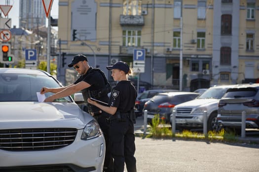 Police patrolman and patrolwoman putting fine for car parking in wrong place. Prevention of traffic rules violation