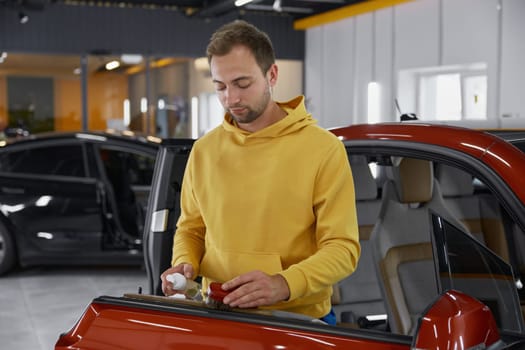 Man brushing leather parts of car door during auto detailing procedure in garage workshop. Cleansing and hygienic polishing of vehicle interior