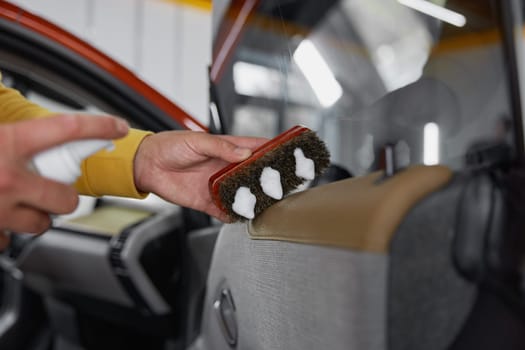 Male master applying disinfectant foam on brush for car detailing in professional wash auto service