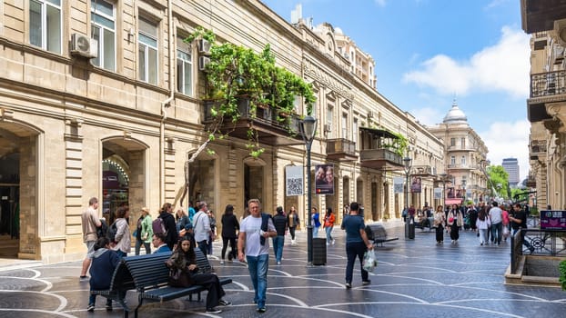Baku, Azerbaijan - May 5, 2024: Nizami Street bustles with activity as pedestrians stroll under a clear blue sky. Lush greenery adorns the balconies, enhancing the vibrant atmosphere