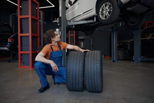 Repairman rolling car spare tires while working on wheel replacement providing professional automotive mechanical