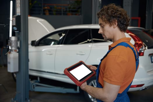Portrait of male car technician looking at computer tablet while working with auto breakage at repair service station