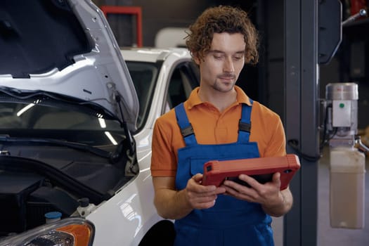 Portrait of serious male car technician looking at computer tablet while working with auto breakage at repair service station