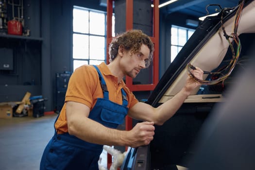 Male auto electric checking car cables and electrical system while working at automotive repair station