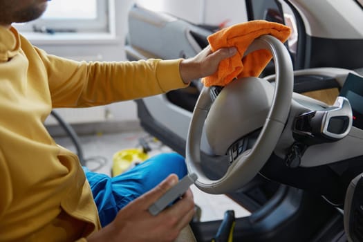 Cropped photo of man hands disinfecting car steering wheel holding antiseptic bottle wiping surface with cloth