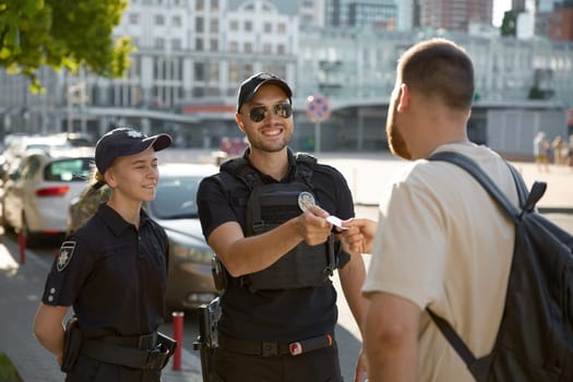 Friendly smiling patrol policeman giving back passport to citizen after checkup on city street. Law, order and protection of civilian