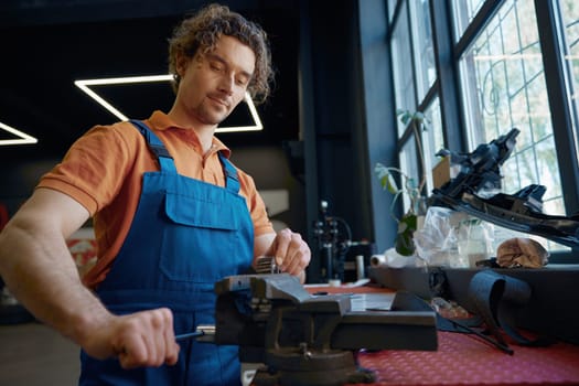 Auto mechanic using bench vice to adjust spare part at car repair garage. Automotive repairman everyday routine and professional occupation