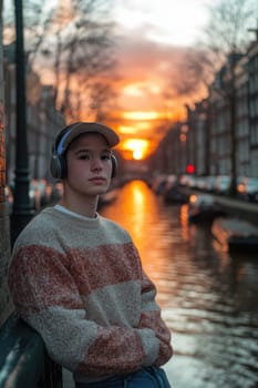 A young man leaning against a wall near the canals, wearing an oversized sweater and a baseball cap, listening to music through his vintage headphones. AI generative.