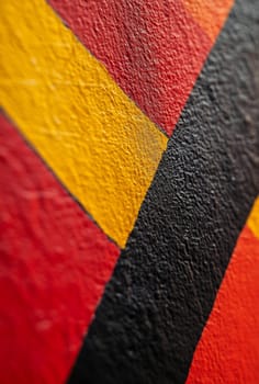 Close-up view of a textured wall painting featuring vibrant red, yellow, and black geometric shapes in an urban setting.