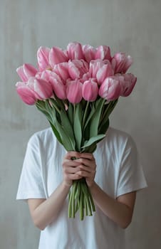 A person stands indoors, presenting a sizable bouquet of pink tulips, showcasing their vibrant color and fresh beauty.