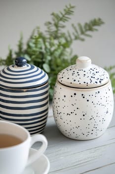 Two decorative ceramic containers with a tea cup and greenery create a cozy atmosphere in a modern setting.