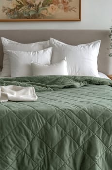 A neatly made bed features a soft green quilted cover and fluffy white pillows, creating a tranquil and inviting atmosphere.