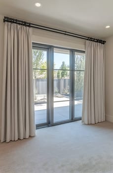A spacious living room showcasing soft, light-colored curtains framing a bay window that opens to a serene outdoor space.
