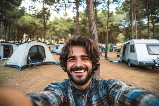 A joyful camper takes a selfie in a lush forest campsite filled with tents and trailers during a sunny day.