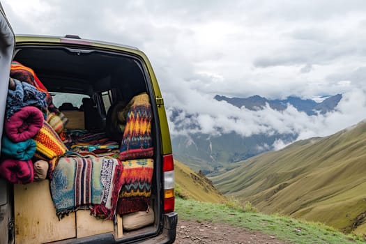 A van filled with vibrant blankets is parked at a scenic mountain viewpoint with clouds rolling in.
