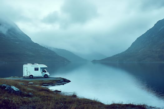 A white RV parked by a calm lake, surrounded by misty mountains during the early morning light.