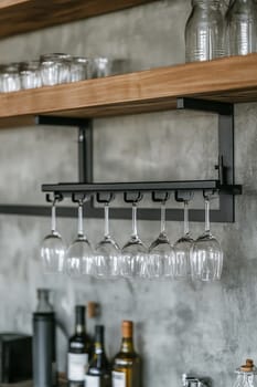 A stylish arrangement of wine glasses suspended from a sleek rack above a modern kitchen countertop with various bottles below.