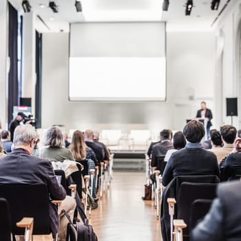Speaker giving a talk in conference hall at business event. Rear view of unrecognizable people in audience at the conference hall. Business and entrepreneurship concept