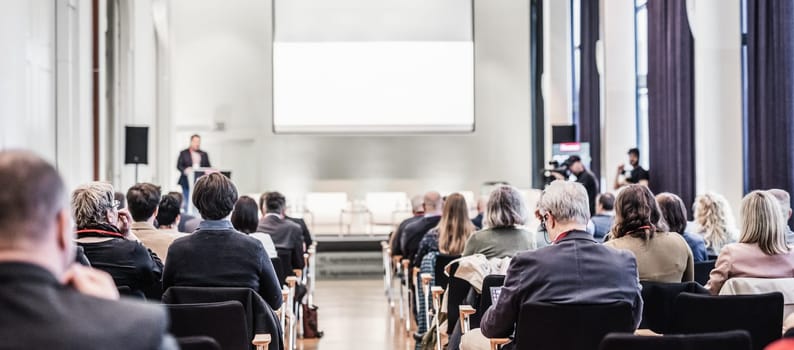 Speaker giving a talk in conference hall at business event. Rear view of unrecognizable people in audience at the conference hall. Business and entrepreneurship concept