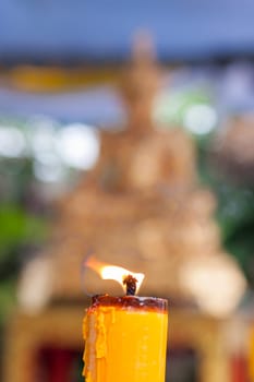 Candlelight burning in front of Buddha statue. Focus on candle frame, buddha blured in background