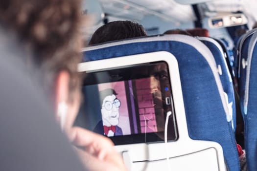 Reflection of a passenger on an airplane touch screen monitor while watching cartoon during long flight. Entertainment service system in aircraft