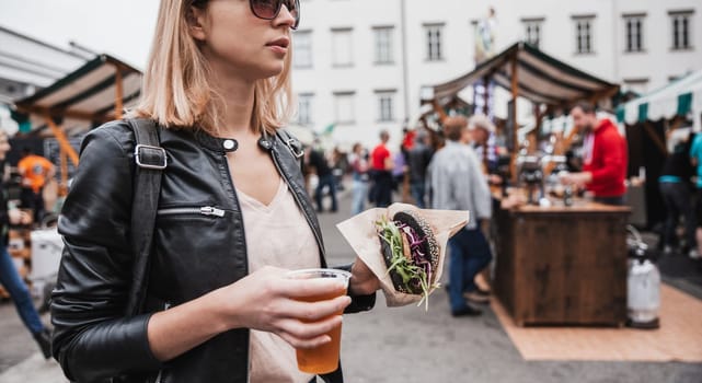 Close up of woman hands holding delicious organic salmon vegetarian burger and homebrewed IPA beer on open air beer an burger urban street food festival in Ljubljana, Slovenia