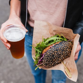 Close up of woman hands holding delicious organic salmon vegetarian burger and homebrewed IPA beer on open air beer an burger urban street food festival in Ljubljana, Slovenia