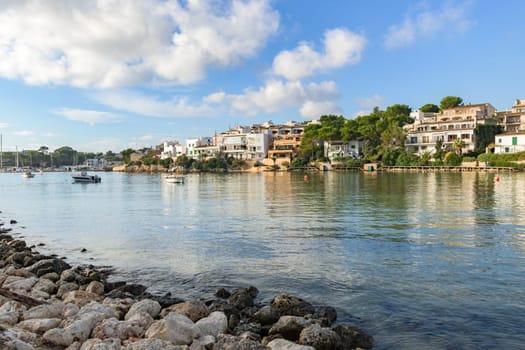 Coastal town with clear water and buildings reflected under a vibrant blue sky, porto petro, mallorca balearic islands, spain