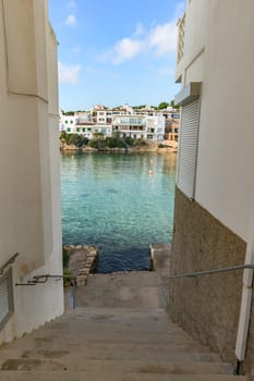 View of a coastal town through a staircase leading to clear waters under a blue sky, porto petro, mallorca balearic islands, spain