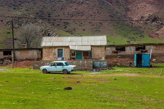 old classic soviet white sedan car in front of rustic farm house in Kyrgyzstan.