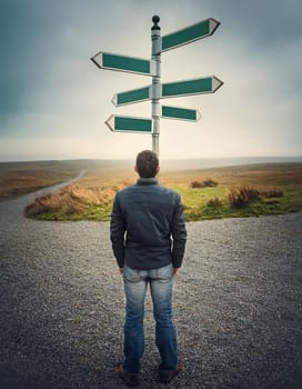 Rear view person stands at crossroad facing a signpost with multiple blank directional signs in a foggy open land. Different way choices, difficult decision, uncertainty concept