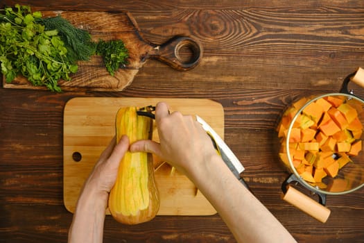 A person skillfully peels a butternut squash, surrounded by fresh herbs and diced squash. The warm wood tones of the kitchen create a welcoming atmosphere for cooking.