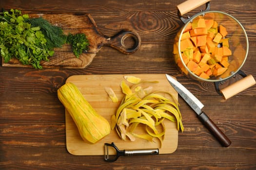 Fresh butternut squash is being peeled and chopped on a wooden cutting board, accompanied by vibrant herbs and tidy kitchen tools. The ambiance is bright and inviting, perfect for cooking.
