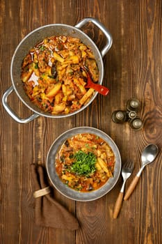 Top view of a warm vegetable stew, rich with various ingredients in a bowl beside a pot. Fresh herbs garnish the dish, creating an inviting meal on a rustic wooden surface.