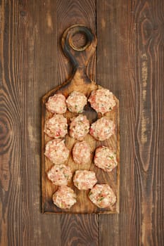 A wooden cutting board showcases a dozen freshly made meatballs, blending ground meat and herbs. The rustic texture of the board complements the delightful presentation in a warm kitchen setting.