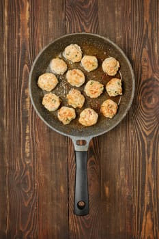 Meatballs are sizzling in a skillet on a rustic wooden table, showcasing a delicious cooking process. The dish highlights various spices and herbs, contributing to a flavorful meal preparation.