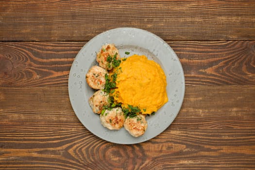 Top view of a plate with golden-brown meatballs garnished with herbs alongside a creamy mashed pumpkin