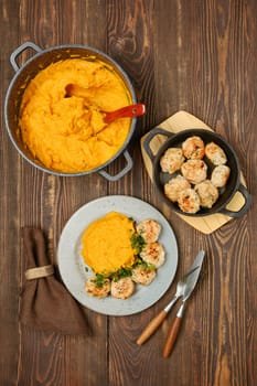 A hearty meal featuring creamy mashed pumpkin and turkey meatballs, elegantly plated on a rustic wooden table, top view