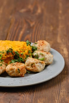 Close-up view of a plate with freshly made meatballs garnished with herbs alongside a serving of smooth, creamy mashed pumpkin