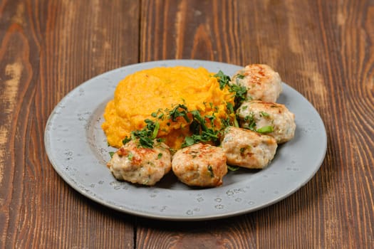 Juicy meatballs made from ground meat with a mound of smooth and creamy mashed pumpkin, garnished with fresh herbs