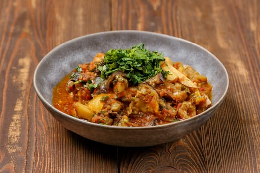 A rich and flavorful vegetable stew is served in a rustic bowl, topped with fresh herbs. The dish features various vegetables and herbs, showcasing vibrant colors and inviting aromas.
