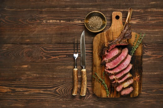 Succulent slices of tomahawk steak are arranged neatly on a rustic wooden cutting board, accompanied by fresh herbs and utensils. The scene captures a delicious meal prepared with care.