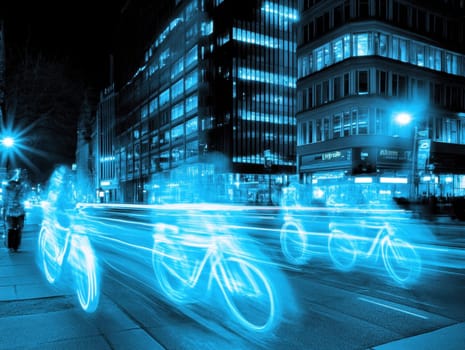 Cyclists riding down a city street at night, leaving blue light trails in a long exposure