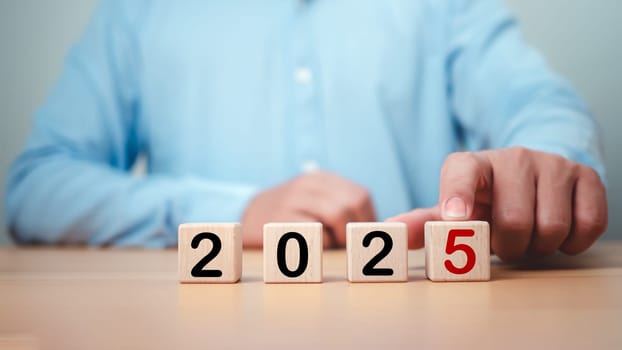 Businessman selected cube from 2025 on wooden table, Planning 2025 trends new year symbol, Concept words 2025 start on beautiful wooden blocks, Business 2025 target new year concept. Copy space.