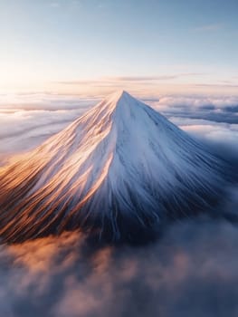 Majestic snow covered mountain peak rising above clouds at sunrise, with dramatic golden light illuminating its slopes.