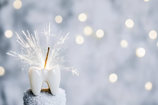 A decorative cake topper shaped like a tooth with sparklers adding a festive touch to a celebration in a blurred background.
