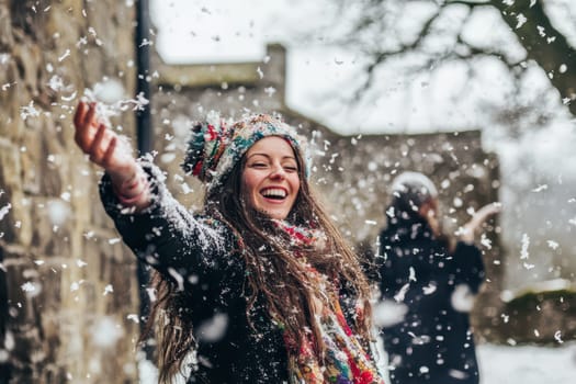 A happy woman is embracing the snowfall smiling and laughing with snowflakes surrounding her in a winter setting.
