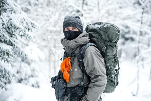 A person stands in a snowy forest wearing warm clothing and a large backpack showcasing a winter hiking adventure in a cold environment.